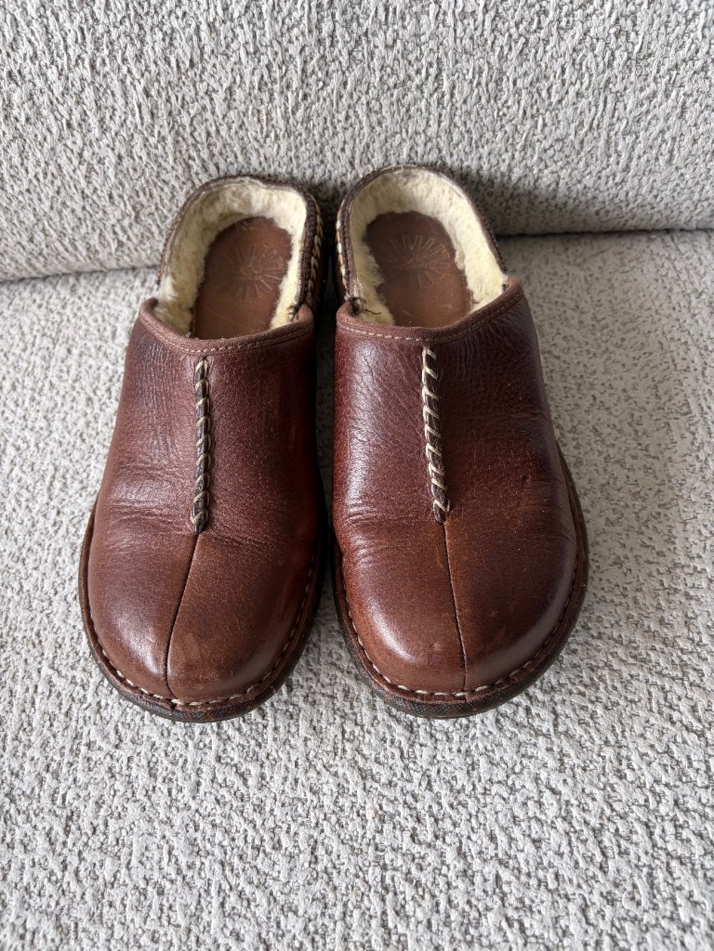 UGGS brown leather slip-on clogs with fleece lining.